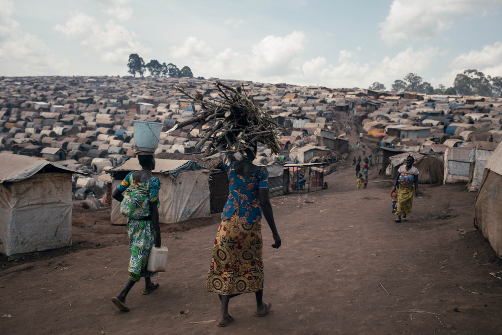 Des femmes traversent le camp de déplacés de Plaine Savo, transportant du bois et de l'eau.