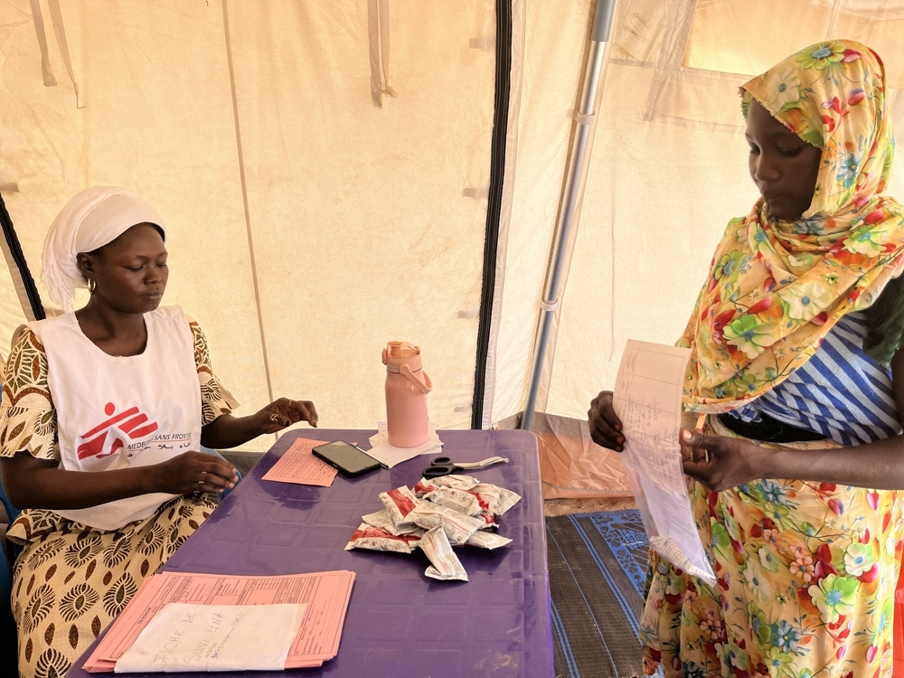 Une travailleuse sociale de MSF distribue Plumpy'Nut, un aliment thérapeutique prêt à l'emploi (ATPE), à une mère dans la clinique mobile installée sur le site de transit d'Adémour, dans la province de Sila, au Tchad. Cette distribution essentielle a permis de prévenir et de traiter la malnutrition aiguë chez les jeunes enfants touchés par la crise des déplacements de population. Chad, Juin 2026