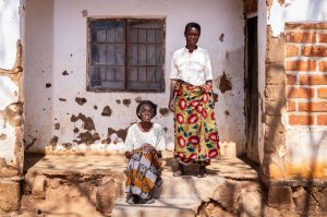 Grace Nyambi, 72 ans, et sa fille devant leur domicile à Chileka, dans le district de Blantyre, le 21 juillet 2026. Mère de quatre enfants, elle bénéficie depuis trois mois d'une aide financière mensuelle, utilisée en priorité pour acheter du maïs destiné à la préparation du *nsima*, un plat local. Malawi ©Jérémy Lampin