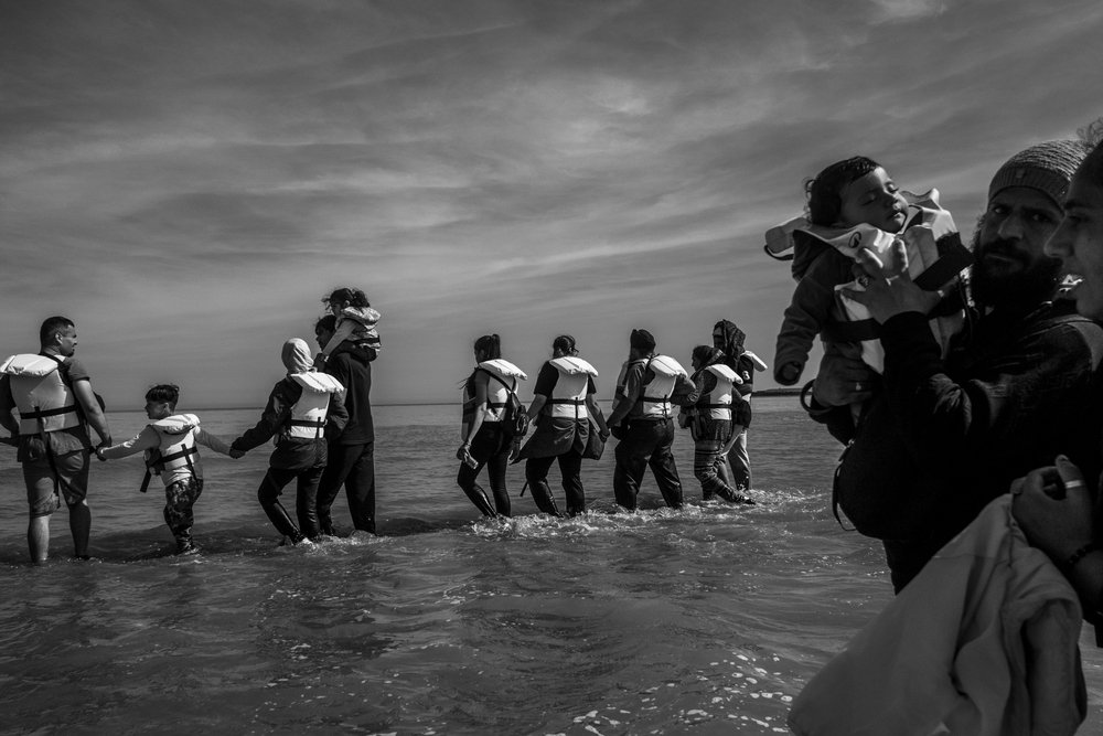 Un groupe d’exilés progresse dans l’eau pour rejoindre un bateau pneumatique, dans le but de traverser la Manche, à Grand-Fort-Philippe, en France. Juin 2026, Calais, France ©Michael Bunel